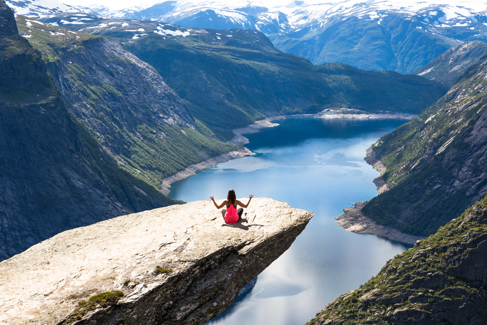 Sport woman posing on Trolltunga. Happy woman enjoy beautiful lake and good weather in Norway.